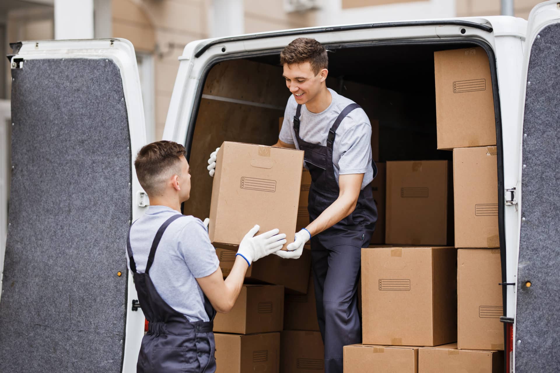 two young handsome movers wearing uniforms are unloading the van full of boxes house move mover 2 e1694426476985